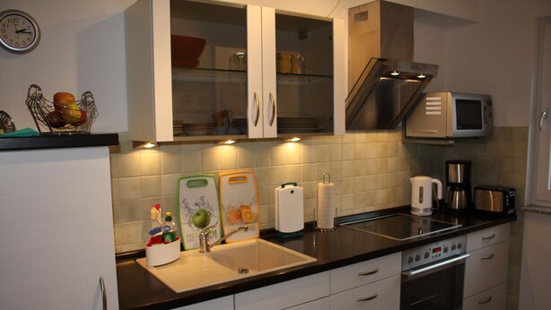 A kitchen with white cabinets, a black countertop, a stainless steel microwave, a coffee maker, and a sink. - Strandnahe 3-zimmer-fewo im 3.og für 4 Pers. mit Wlan (Graal-Müritz)