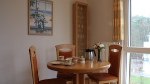 A dining area with a round table, four chairs, a coffee pot, cups, and a vase with flowers. - Strandnahe 3-zimmer-fewo im 3.og für 4 Pers. mit Wlan (Graal-Müritz)