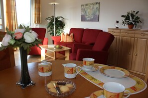 Un coin repas avec une table dressée pour quatre personnes, comprenant des assiettes, des tasses et un vase rempli de fleurs.