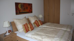 A bedroom with a bed, pillows, a nightstand, a lamp, and a wooden wardrobe. - Strandnahe 3-zimmer-fewo im 3.og für 4 Pers. mit Wlan (Graal-Müritz)