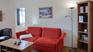 A room with a red sofa, a wooden coffee table with cups, a bookshelf, and a painting on the wall. - 2-zi-fewo für 4 Pers. mit Wlan, Haustiere Erlaubt (Graal-Müritz)