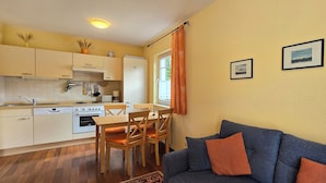 A compact kitchen with modern appliances, a dining area with wooden chairs, and a blue sofa with orange cushions. - 2-zimmer-fewo für 3 Pers. Inkl. Strandkorb (Graal-Müritz)