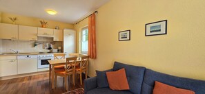 A compact kitchen with modern appliances, a dining area with wooden chairs, and a blue sofa with orange cushions. - 2-zimmer-fewo für 3 Pers. Inkl. Strandkorb (Graal-Müritz)