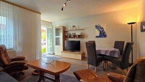 A modern living room with a sofa, leather chairs, a wooden coffee table, a TV, and a dining area with a table and chairs. - 2-zi.-fewo im EG mit Terrasse im Ortszentrum (Graal-Müritz)