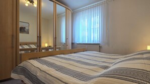 A bedroom with a large bed, a wardrobe, a window with curtains, and a bedside lamp. - 2-zi.-fewo im EG mit Terrasse im Ortszentrum (Graal-Müritz)