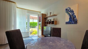 A dining area with a round table, two chairs, a television, and a shelf with decorative items. - 2-zi.-fewo im EG mit Terrasse im Ortszentrum (Graal-Müritz)