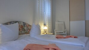 Een hotelkamer met twee bedden, witte beddengoed, een bloemen hoofdbord, een witte stoel en een lamp.