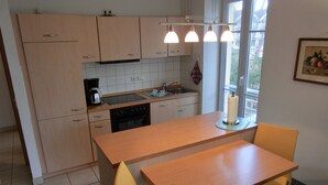 Een compacte keuken met lichte houten kastjes, een centraal eiland, een spoelbak en een raam met uitzicht.