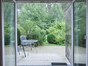 Puerta de vidrio que da a un patio con mesa y sillas, rodeado de abundante follaje.