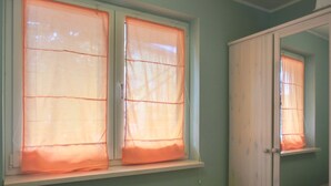 Quarto com duas janelas cobertas por cortinas laranja, um guarda-roupa branco e uma parede verde.