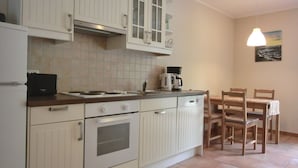 Cozinha com armários brancos, fogão Bosch e cafeteira. Há uma mesa de jantar com cadeiras e um quadro na parede.