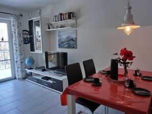 Uma área de refeições com uma mesa vermelha, cadeiras, um globo, uma TV e uma estante com livros e objetos decorativos.