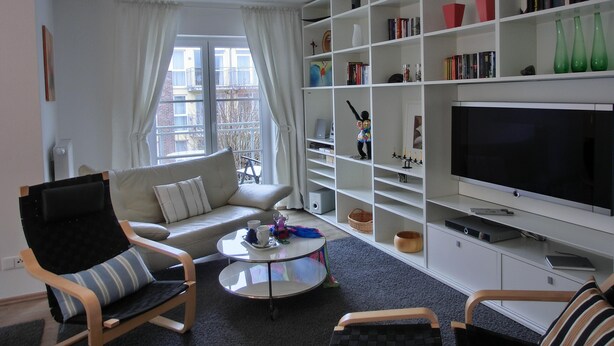 Una sala de estar moderna con un sofá, sillones, una mesita de centro y una estantería llena de libros y objetos decorativos.