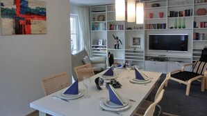 Un comedor con una mesa blanca dispuesta para cuatro personas, rodeada de sillas de mimbre. Tres lámparas colgantes iluminan la mesa.