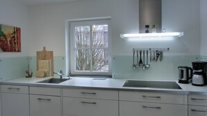 Una cocina moderna con armarios blancos, un lavamanos de acero inoxidable, una ventana con vistas a árboles desnudas y un colgador para utensilios.