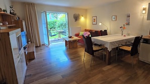Een moderne keuken met houten kastjes, een eethoek met tafel en stoelen, en een schuifdeur die leidt naar een terras met tuinmeubilair.