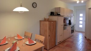 Un comedor con una mesa dispuesta para cuatro personas, un aparador de madera y una cocina al fondo.
