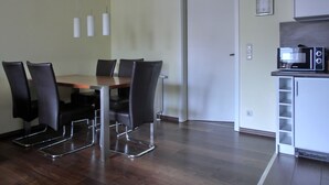 A dining area with a wooden table and black chairs, a kitchen with a microwave, and a white cabinet. - 3-zi.-fewo für 4+2 Personen - mit Telefon- und Internetanschluss (Graal-Müritz)