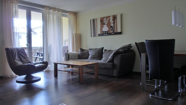 A living room with a sofa, a coffee table, a chair, and a dining table. There is a painting on the wall and a window with curtains. - 3-zi.-fewo für 4+2 Personen - mit Telefon- und Internetanschluss (Graal-Müritz)