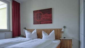 A neatly made bed with white linens, a wooden headboard, and a red abstract painting on the wall. - 3-zi.-fewo für 4+2 Personen - mit Telefon- und Internetanschluss (Graal-Müritz)