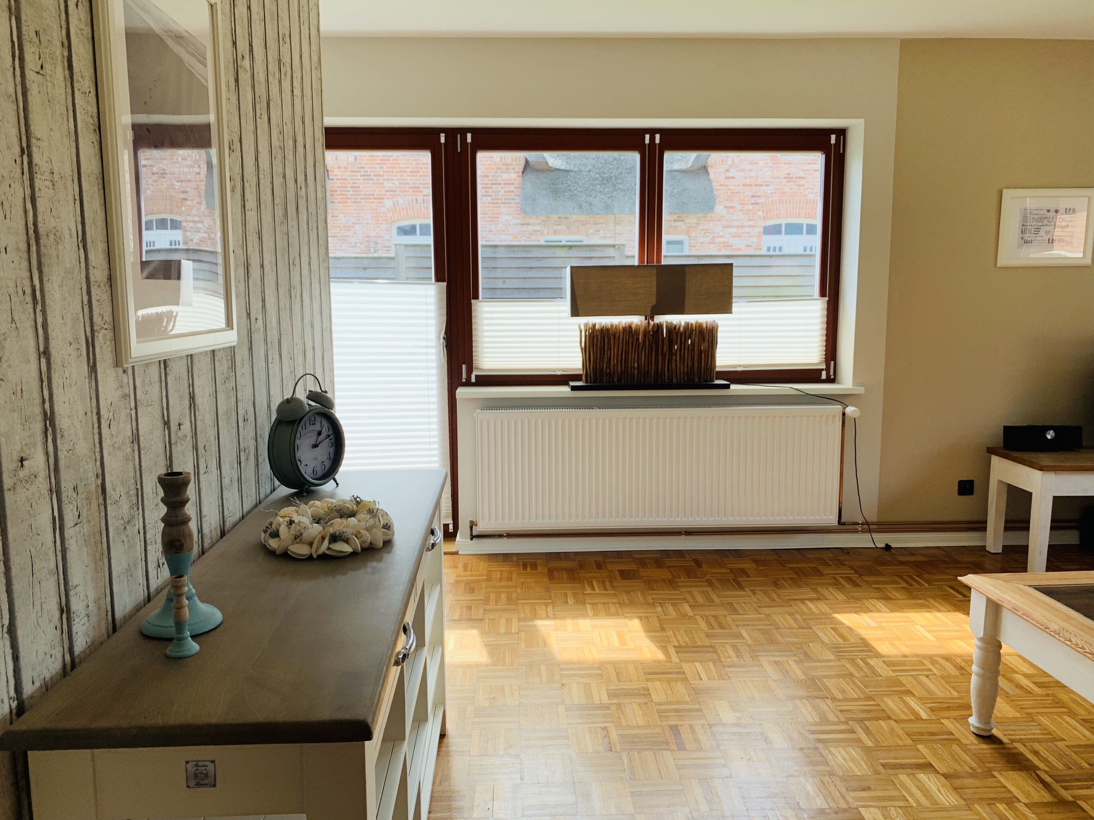 A room with a wooden floor, a radiator, a clock, and a window with blinds.