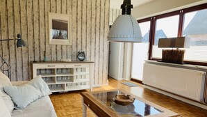 Un salon doté d’un plancher en bois, d’un canapé blanc, d’une table basse en verre, d’une console blanche, d’une horloge murale et d’une fenêtre offrant une vue.