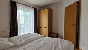 A hotel room with a bed, a wooden wardrobe, and a door. - Ruhige, Strandnahe 2-zimmer-ferienwohnung für 2 Pers. mit Balkon (Graal-Müritz)
