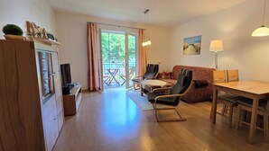 A cozy living room with a wooden dining table, chairs, a sofa, and a TV. - Ruhige, Strandnahe 2-zimmer-ferienwohnung für 2 Pers. mit Balkon (Graal-Müritz)