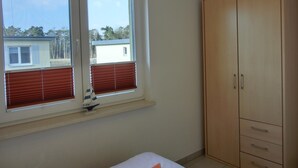 Un dormitori amb una finestra gran, un armari i una taula petita amb un objecte decoratiu.
