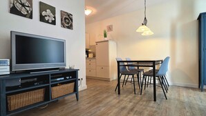 En stue med et fladskærms-tv, et spisebord med stole, et køkkenområde og et skab med glas.