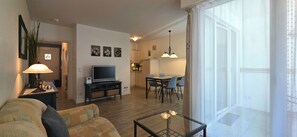 A living room with a sofa, a TV, and a glass coffee table. There is a dining area with a table and chairs.