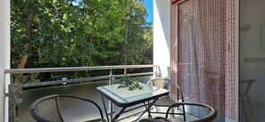 A balcony with a glass table and chairs, a potted plant, and a view of trees.