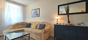 A living room with a sofa, a glass coffee table, a lamp, a dresser, and a framed picture on the wall. - Strandnahe 2-zimmer-fewo im 1. OG für 3 Pers (Graal-Müritz)