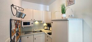 Een kleine keuken met witte kastjes, een magnetron, een waterkoker en een spoelbak.