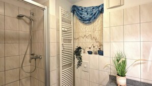 Ein Badezimmer mit Dusche, Handtuchhalter und einer Topfpflanze.