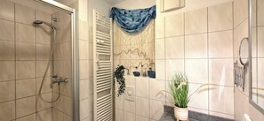 Une salle de bain avec une douche, un porte-serviettes et une plante en pot.