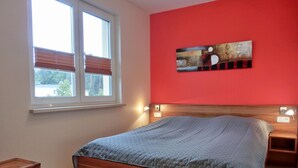 A bedroom with a wooden bed, a red wall, a window with blinds, and a painting above the bed.