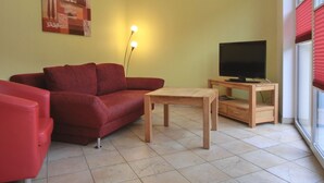 A living room with a red sofa, a wooden coffee table, a TV on a wooden stand, and a painting on the wall.