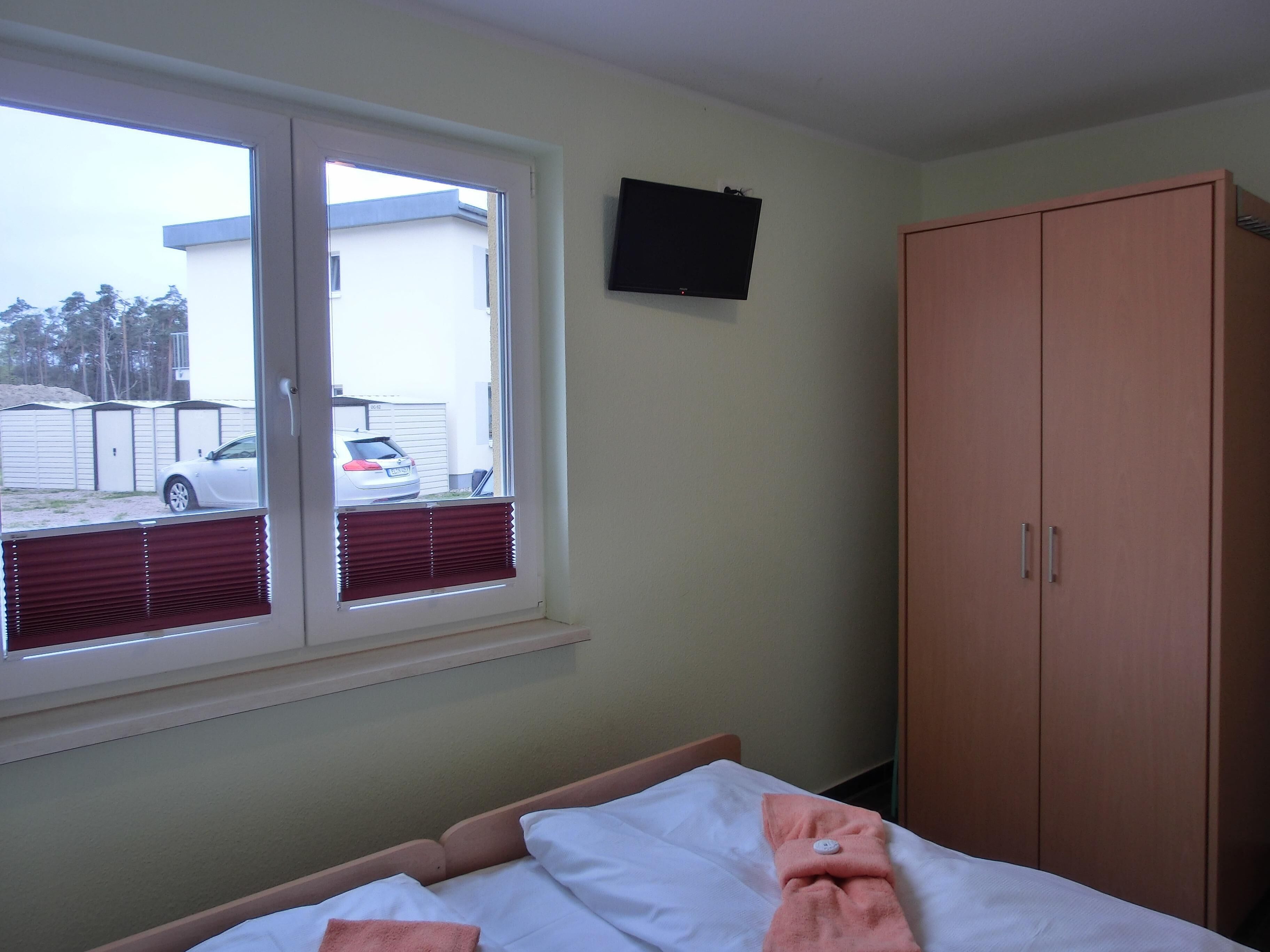 Un dormitorio con cama, ventana con persianas, armario y televisión en la pared.