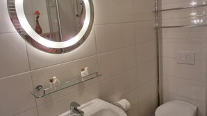 Een badkamer met een ronde spiegel, een wastafel, een toilet en een glazen plankje met toiletartikelen.