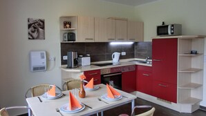 A compact kitchen with modern appliances, a dining area with a table set for four, and a red cabinet. - 2-zimmer-fewo für 5 Pers. EG mit Terrasse (Graal-Müritz)