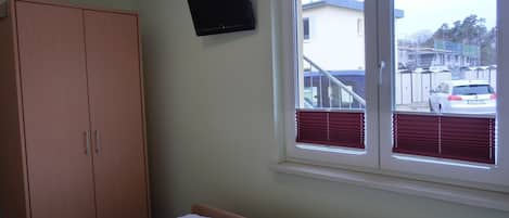 A bedroom with a bed, a wardrobe, a window with blinds, and a television on the wall.