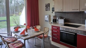 A modern kitchen with a built-in oven, a coffee maker, and a toaster. There is a dining table with chairs and a red curtain. - 2-zimmer-fewo für 5 Pers. EG mit Terrasse (Graal-Müritz)