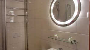A modern bathroom with a glass shower enclosure, a round mirror with a light, and a sink with a glass shelf above it. - 2-zimmer-fewo für 5 Pers. EG mit Terrasse (Graal-Müritz)