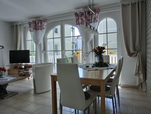 A dining area with a table, chairs, a TV, and a window with curtains. - 3-zimmer-fewo, für 4 Pers. im EG mit Zwei Schlafzimmern (Graal-Müritz)