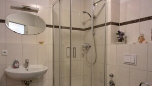 Een badkamer met een douchecabine van glas, een wit wastafelmeubel en een toilet.