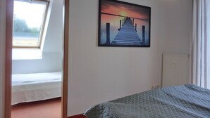 Une chambre à coucher avec un lit, une fenêtre, un tableau représentant une jetée et un luminaire au plafond.