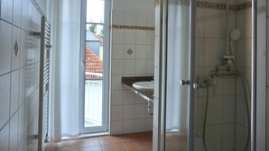 Une salle de bain avec une douche à parois de verre, un lavabo blanc et une porte donnant sur un espace extérieur.