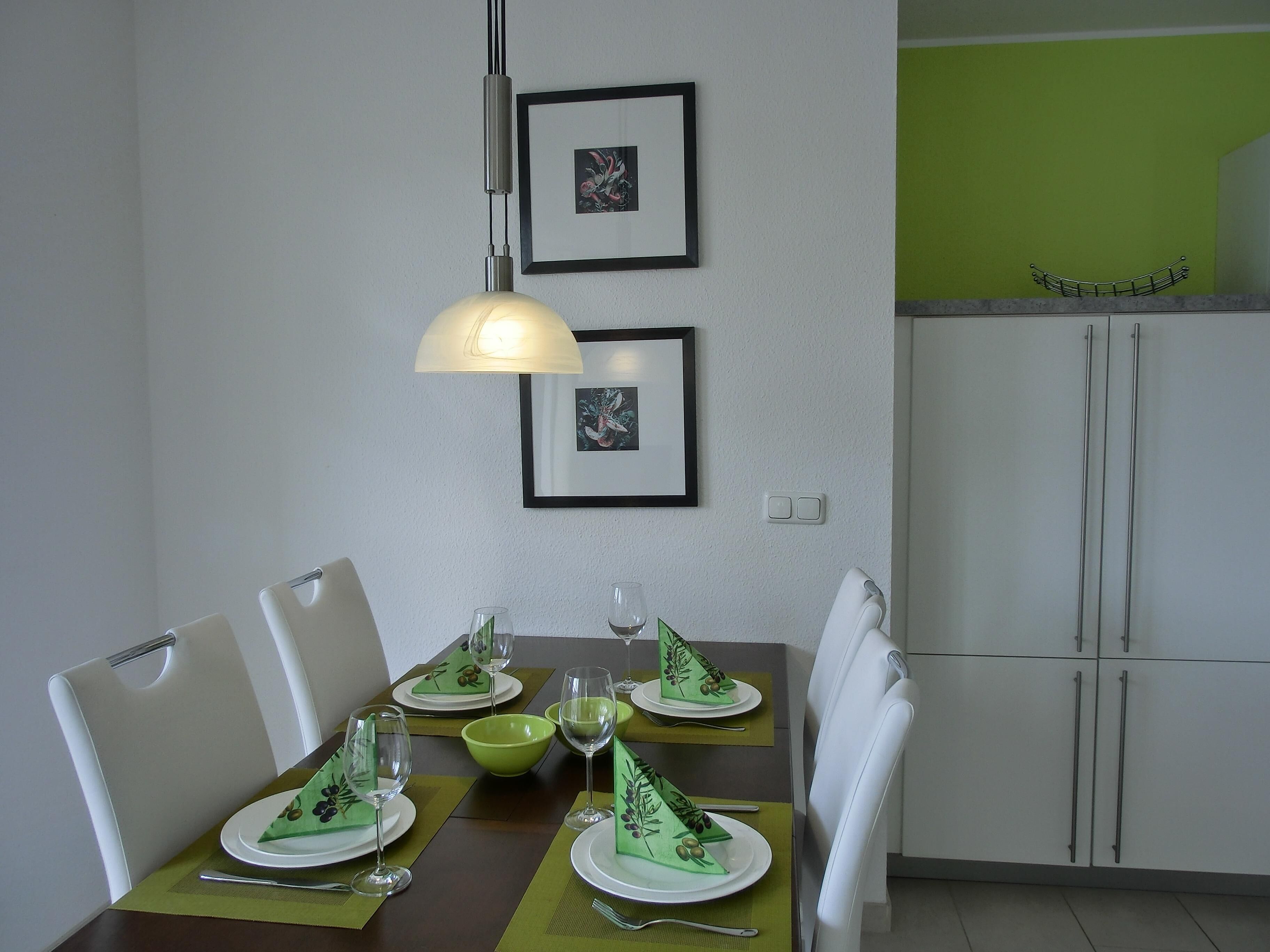 Ein Essbereich mit Tisch für vier Personen, Stühlen, einer Pendelleuchte und gerahmten Bildern an der Wand.