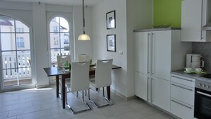 A modern kitchen with white cabinets, a dining area with a table and chairs, and a view of the outside balcony. - 3-zimmer-fewo für 4 Pers. im 1. OG (Graal-Müritz)